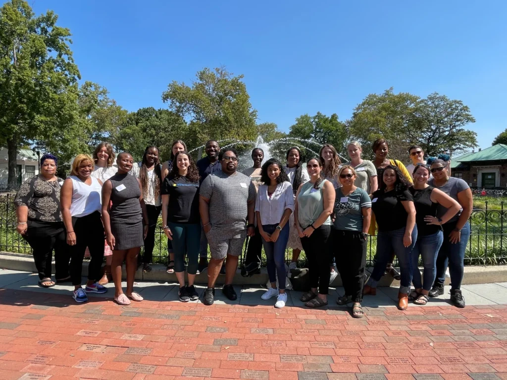 Staff from the Mayor's Office of Civic Engagement and Volunteer Service pose outdoors in front of a fountain. Justin McClearly stands in the front row, fourth from the left, wearing sunglasses and a matching black and white shirt and shorts.