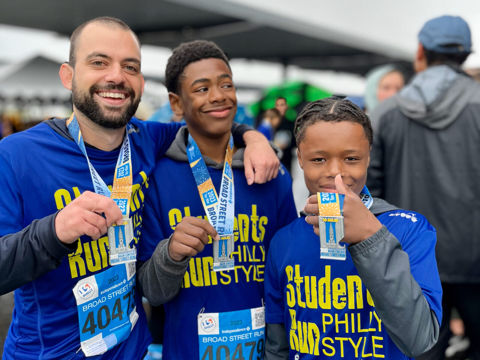 Three people, wearing blue shirts and medals pose while smiling