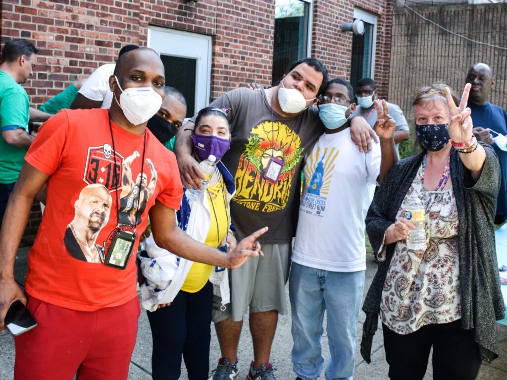 A group of masked people, several of whom are giving peace signs with their hands, pose for a photo