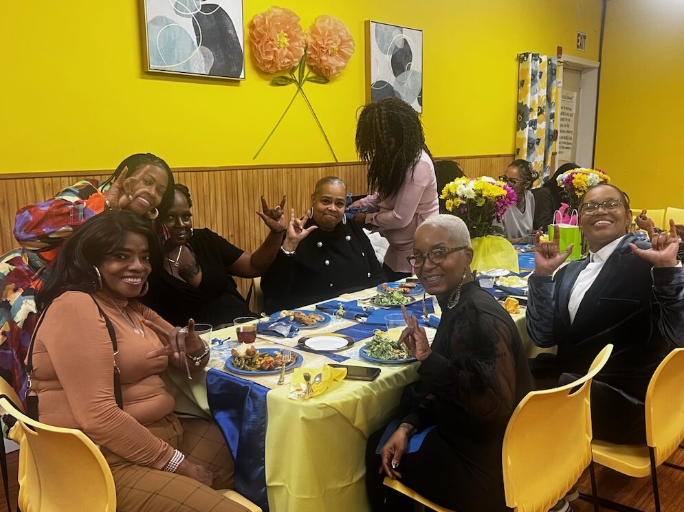 A group of people sit at a table and pose for a photo in a room with yellow walls